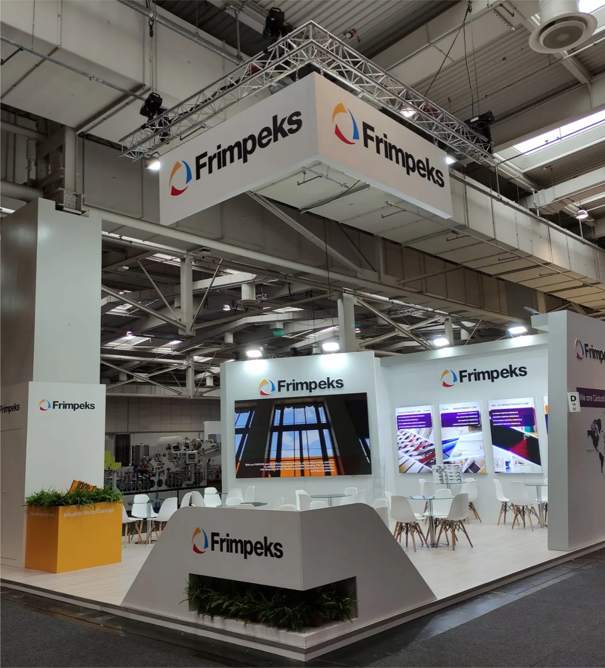Frimpeks standı: truss sisteme asılmış dört cepheli markalı alınlık, açılı karşılama bankosu ve büyük format ekran